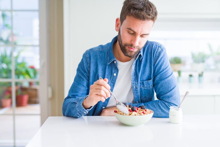 A young man eats a bowl of cereal.