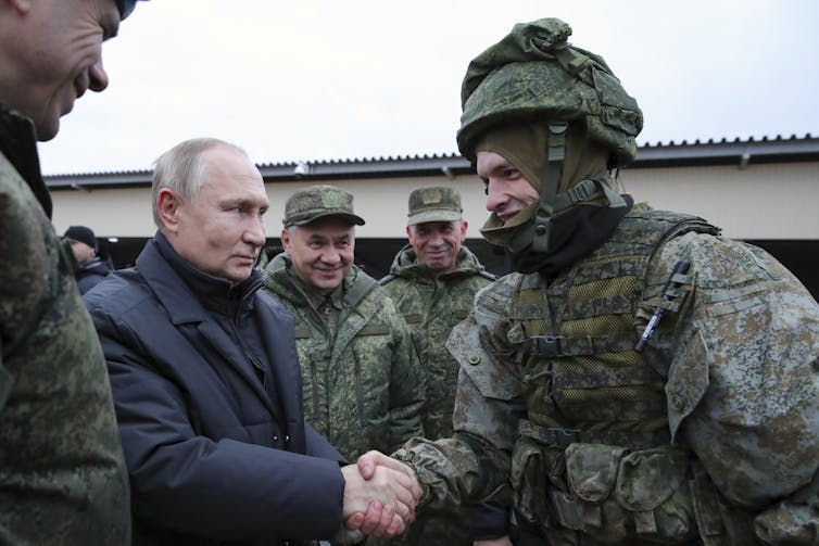 A balding man shakes hands with a soldier in combat gear.