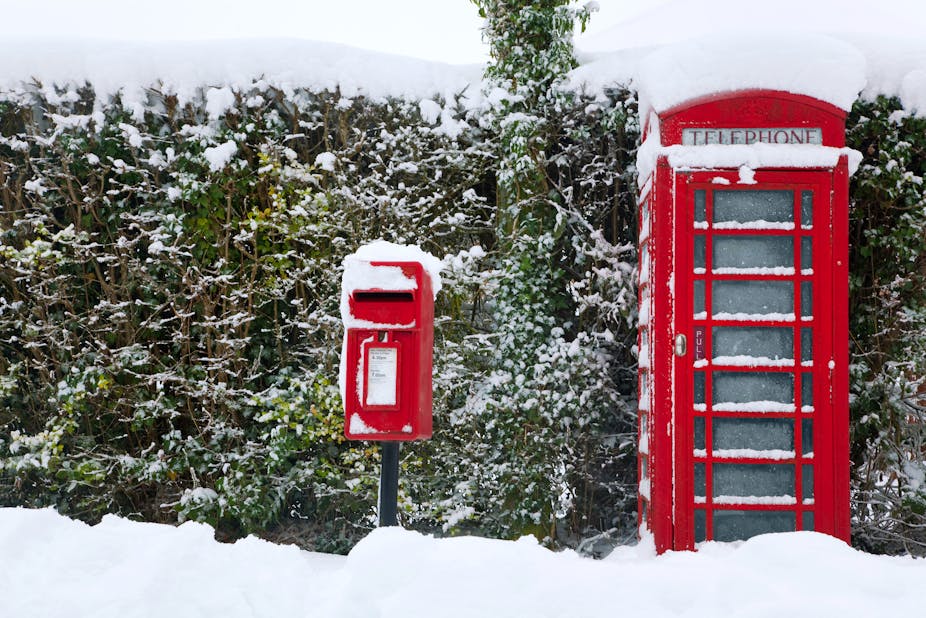 A traditional red English public phone and post box after a heavy snow fall.