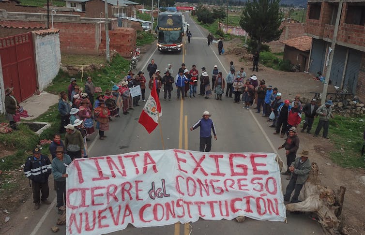 Manifestantes peruanos bloquean una vía principal y sostienen una pancarta pidiendo el cierre del congreso.