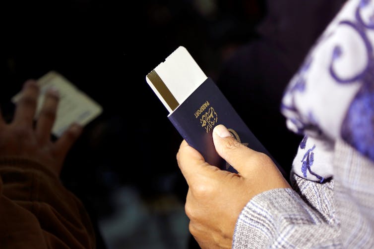 A hand holds a passport and airline ticket.