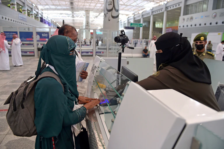 A veiled woman presents her passport to a veiled screener at a counter.