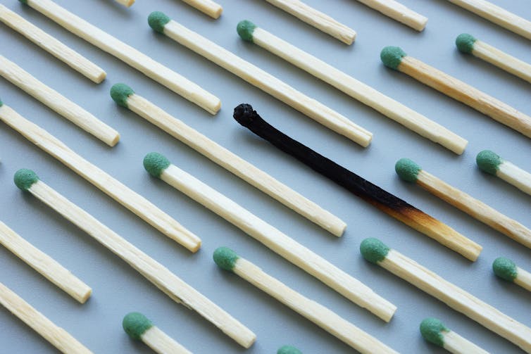 A bunch of unused matches arranged in diagonal, parallel lines on a blue background, with one match completely scorched