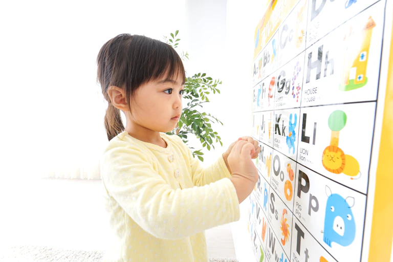 Little girl looking at English alphabet and words on poster