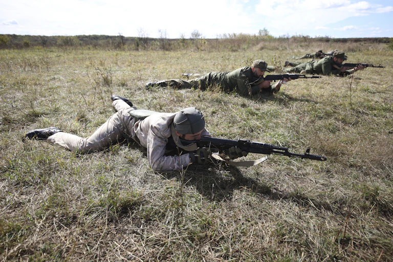 Men in combat gear carrying weapons inch along the ground on their stomachs in a training exercise.
