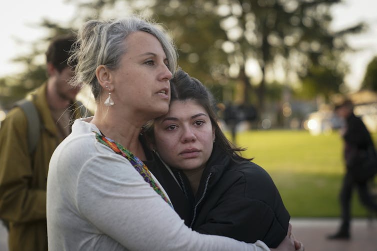Two women embrace each other, one with a tear-stained face, at a daytime gathering to honor the victims killed in the ballroom dance studio shooting in Monterey Park, California.