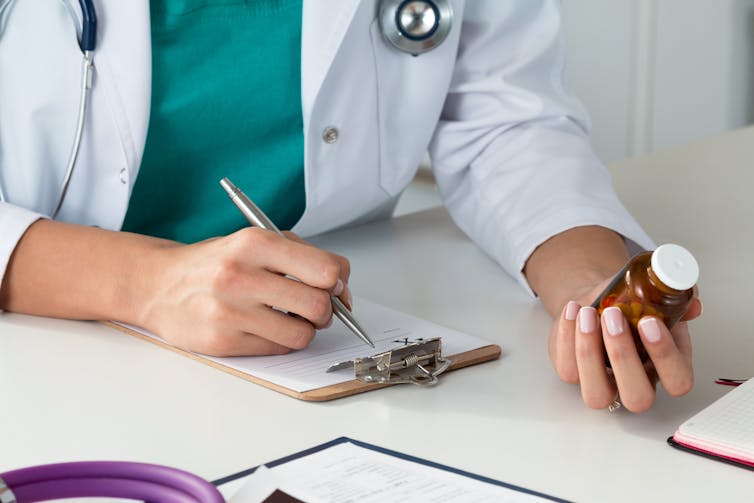 Close-up view of female doctor hand holding bottle with pills and writing prescription