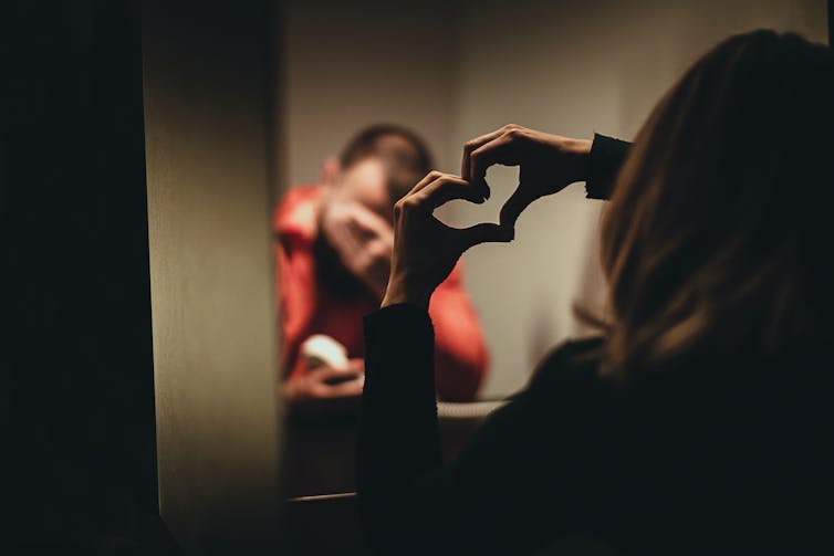 A man in an orange top puts his head in his hands as a woman makes a heart sign with her hands.
