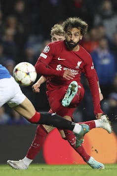Un uomo in divisa da calcio rossa calcia un pallone da calcio.