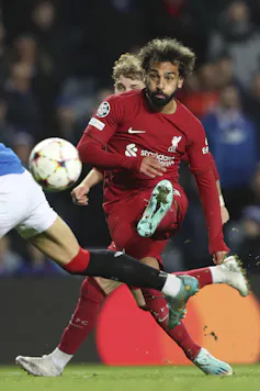 A man in a red soccer outfit kick a football.