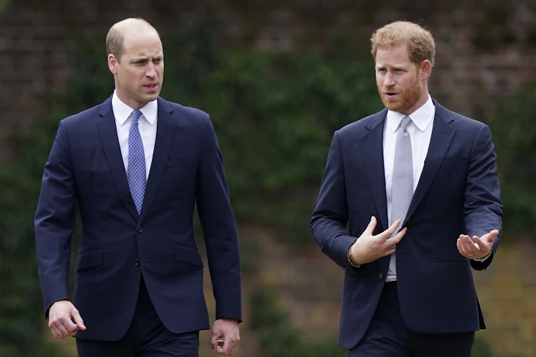Two men in navy suits, one bald and one with red hair, speak as they walk beside each other.