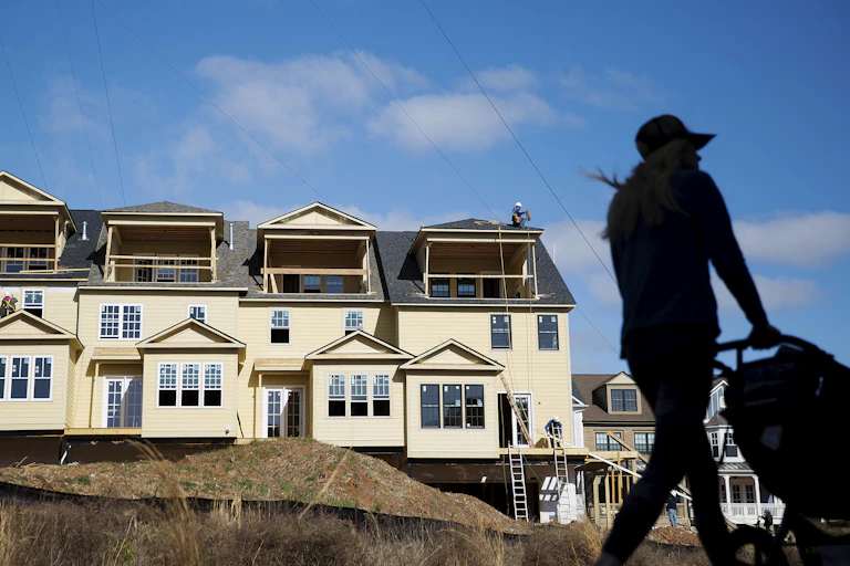 A woman pushes a stroller past four partly-built townhomes