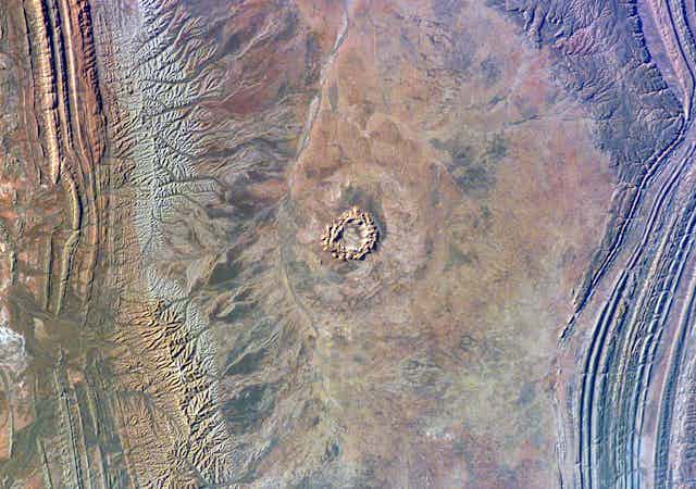 A circular shape on a rocky red landscape seen from high above Earth
