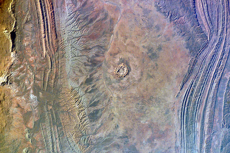 A circular shape on a rocky red landscape seen from high above Earth