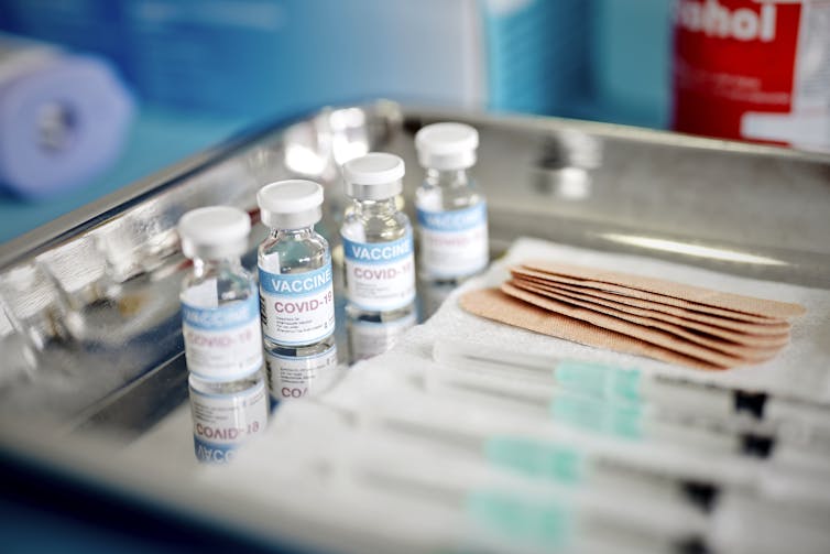 Vials and syringes containing COVID-19 vaccine are displayed on a tray.