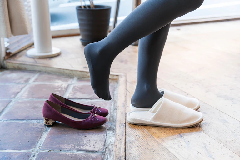 feet stepping out of street shoes into slippers at entrance to home