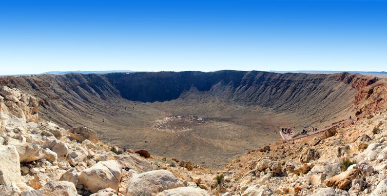 A rocky sand-coloured landscape with a bowl-shaped depression in the middle and a blue sky above it