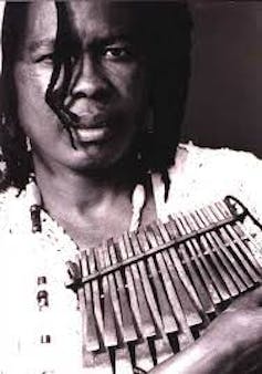 A black and white photo of a woman with dreadlocks holding a musical instrument of wood with metal keys.