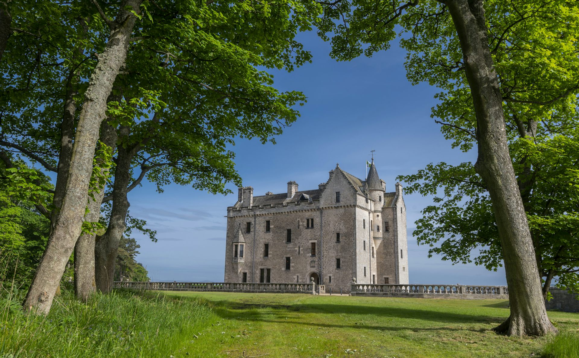 A castle sitting between trees on a bright spring day with a blue sky behind.