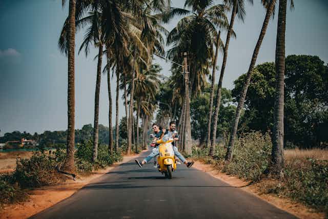 People on scooter with palm trees.