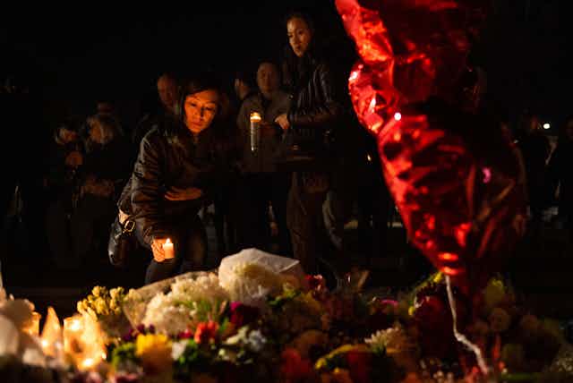 A woman places a candle near some flowers, some red balloons float in the foregrtound.
