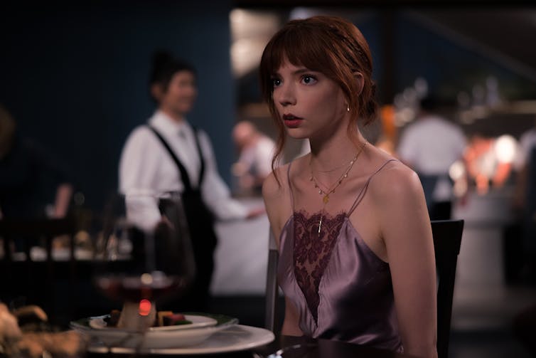 A woman in a pale plum-coloured halter dress stands looking shocked.