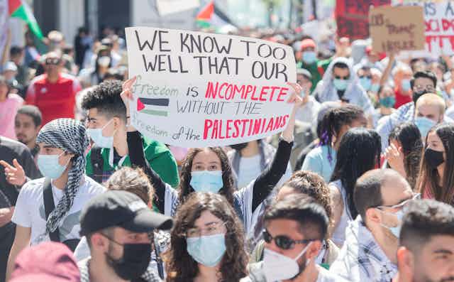 People are seen at a demonstration with one person holding a sign, 'we know too well that our freedom is incomplete without the freedom of the Palestinians.'