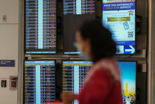 Cancelled flights are seen in red on a digital flight schedules display behind the blurry image of a woman