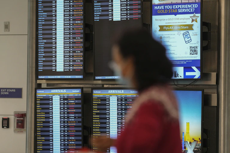 Cancelled flights are seen in red on a digital flight schedules display behind the blurry image of a woman