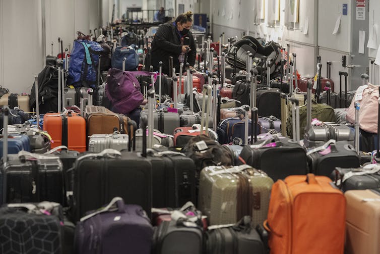 A woman stands in the middle of a wide hallway filled to the brim with suitcases
