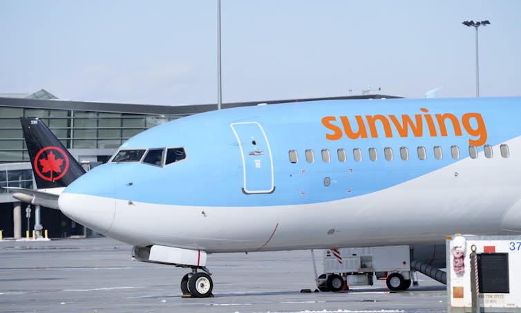 A blue and white plane with the'Sunwing' logo written across the side in orange