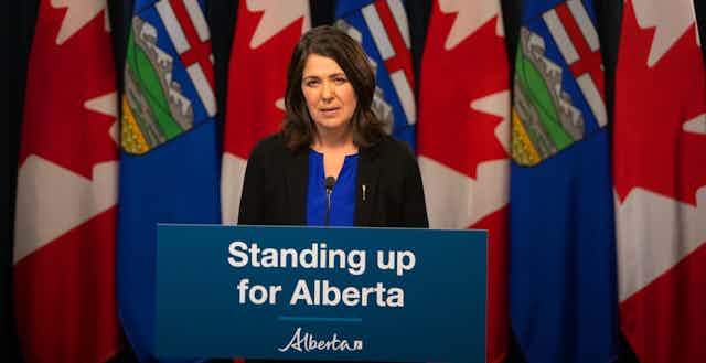 A dark-haired woman speaks from behind a podium that says Standing up for Alberta.