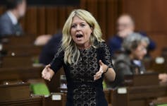 A blonde woman in a black dress gestures as she speaks in the House of Commons.
