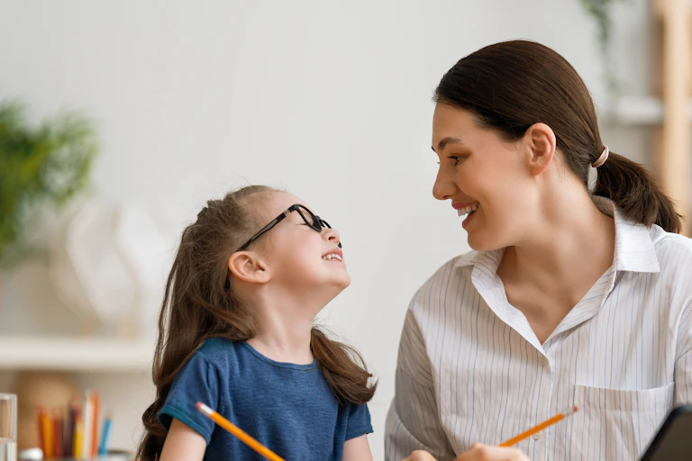 A child and parent sitting with pencils at a table.
