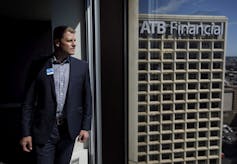 A man stares out a high-rise window with the ATB Financial building seen through the glass.