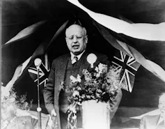 A black-and-white photo of an older bald man, framed by bunting.