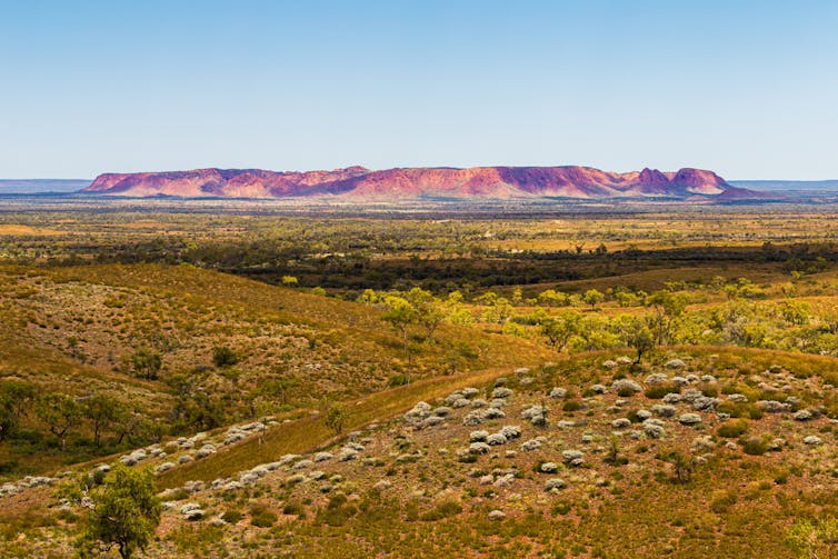 A large red rocky feature on the horizon, with ruddy brown earth in the foreground