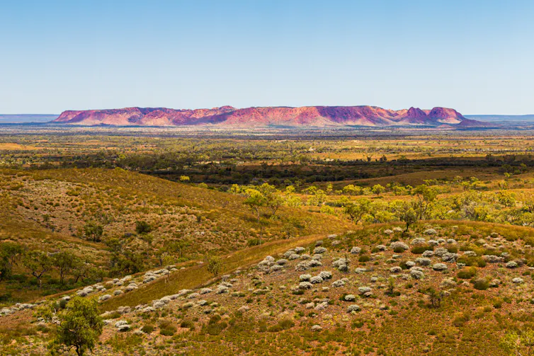 A large red rocky feature on the horizon, with ruddy brown earth in the foreground
