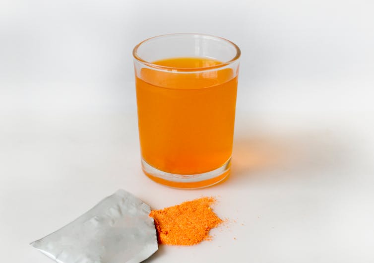 glass of orange liquid and sachet of powder