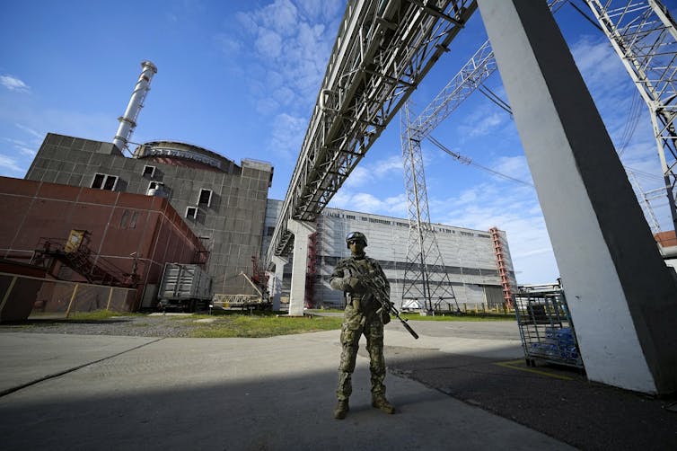 an armed soldier in Russian military uniform stands guard outside a factory