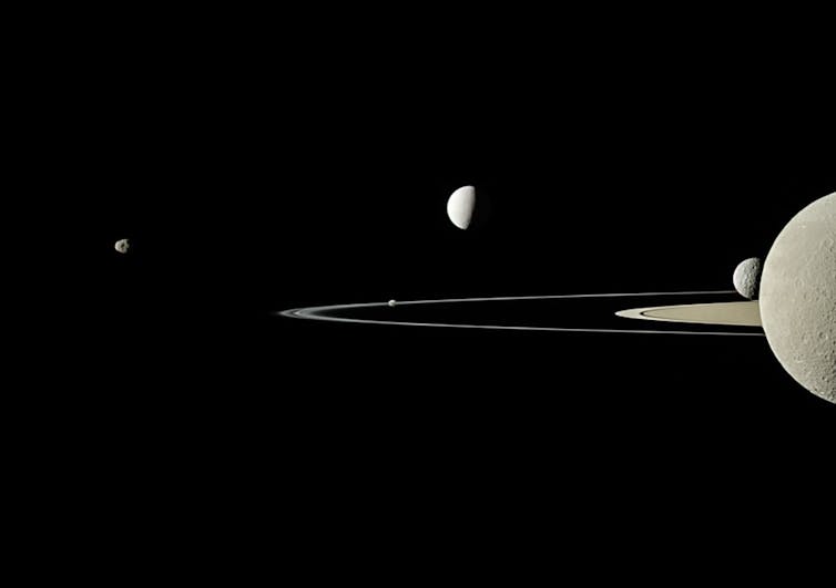 Image of five moons of various sizes and part of Saturn's rings