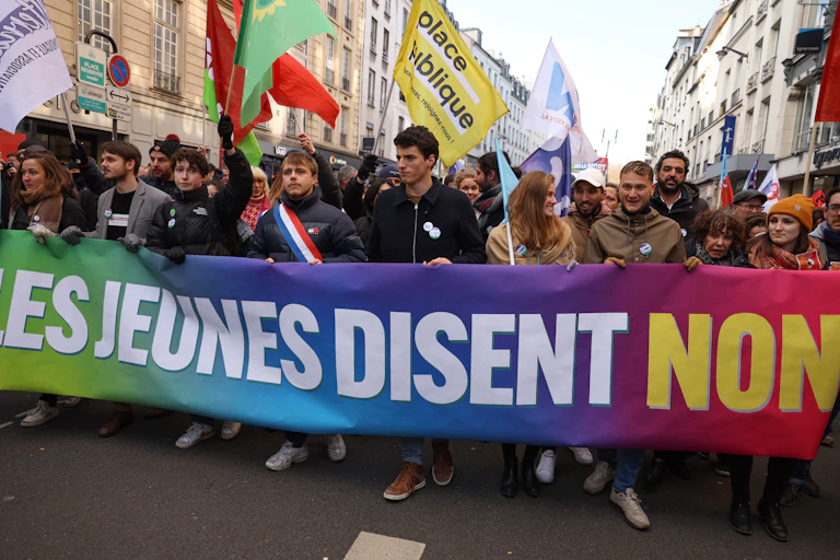 Des manifestants, dont le député du parti de gauche français La France Insoumise (LFI) Louis Boyard (4eL) et le porte-parole de Jeune Garde Antifasciste Raphael Arnault (7eL), tiennent une banderole sur laquelle on peut lire "Les jeunes disent non à la retraite à 64 ans" alors qu'ils participent à un rassemblement, appelé par le parti de gauche La France Insoumise (LFI) et des organisations de jeunesse, pour protester contre la réforme des retraites du Président français, à Paris le 21 janvier 2023.