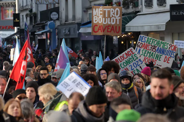 Des manifestants, dont l’un tient une pancarte sur laquelle on peut lire « Métro, boulot, caveau », participent à un rassemblement, appelé par le parti de gauche La France Insoumise (LFI) et des organisations de jeunesse, pour protester contre la réforme de