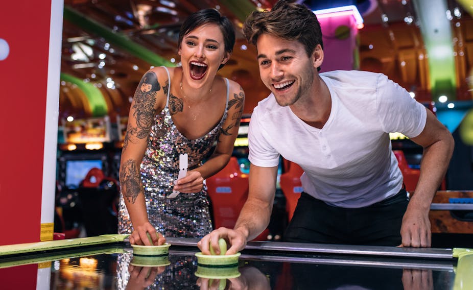 Young couple laughing and playing air hockey in a colourful arcade