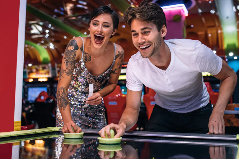Young couple laughing and playing air hockey in a colourful arcade