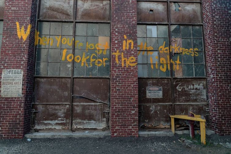 A wall spray painted in yellow with the words 'When you’re lost in the darkness, look for the light'