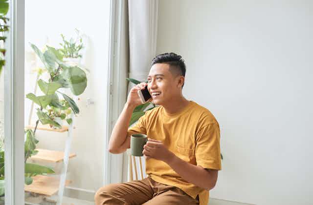 A young man on a phone call holds a mug. 
