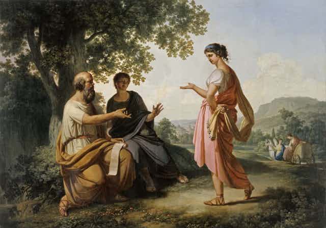 Una mujer de pie habla con dos hombres sentados.