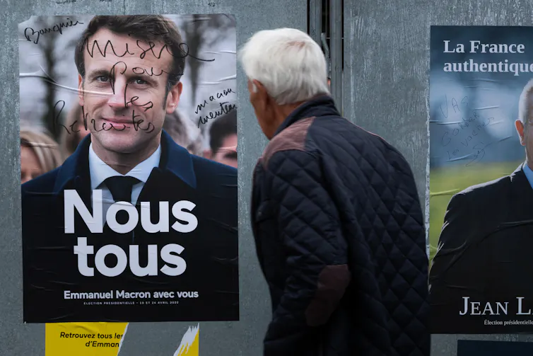 a man looks at a presidential campaign poster of candidate for re-election Emmanuel Macron, on which is written