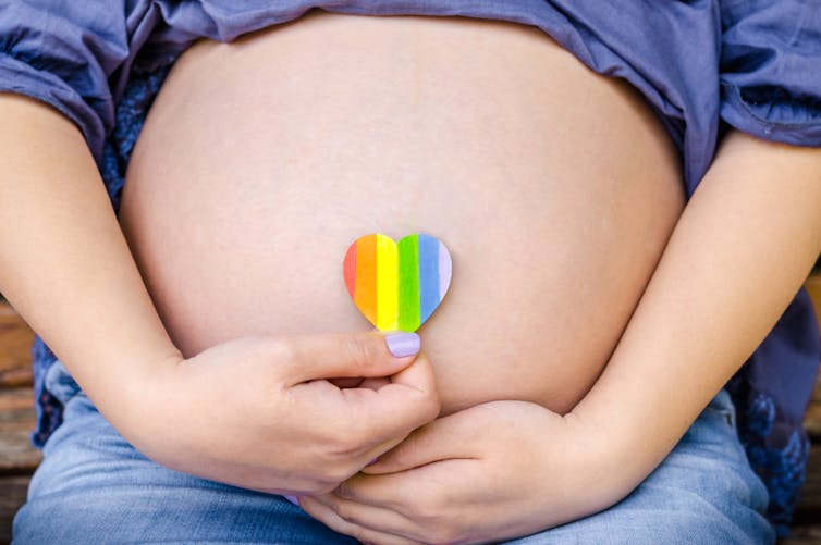 Pregnant belly with hand holding up pride sticker over bellybutton